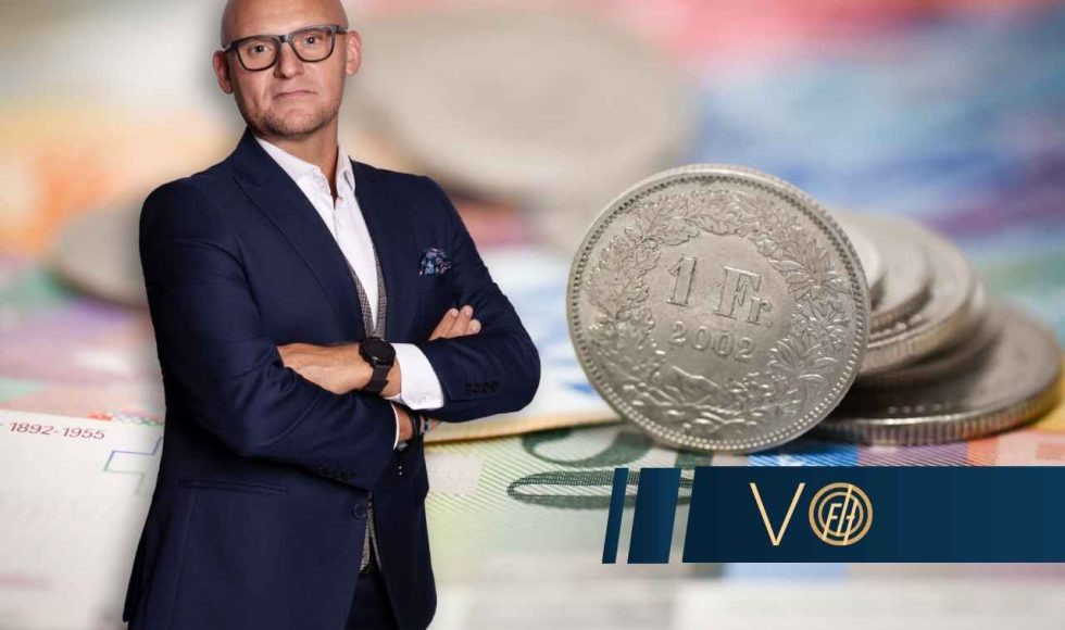 Paweł Wójcik z Votum Finance Help stoi na tle rozmazanych banknotów z dużą, srebrną monetą 1 franka szwajcarskiego