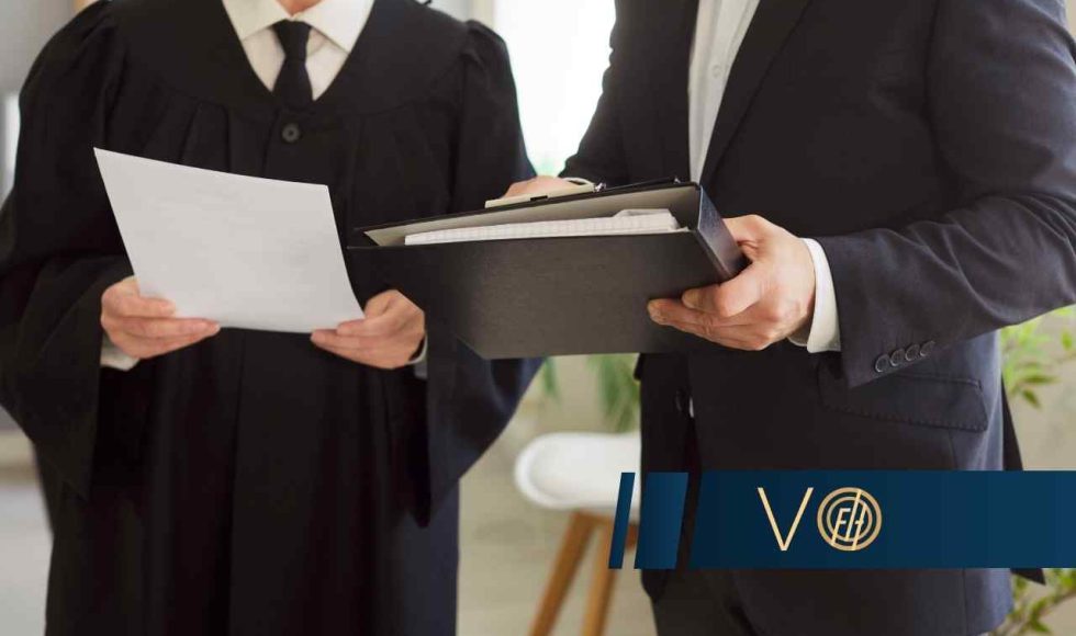 Na zbliżeniu widoczna jest kobieta w todze sędziowskiej oraz mężczyzna w garniturze, przeglądający dokumenty na clipboardzie
