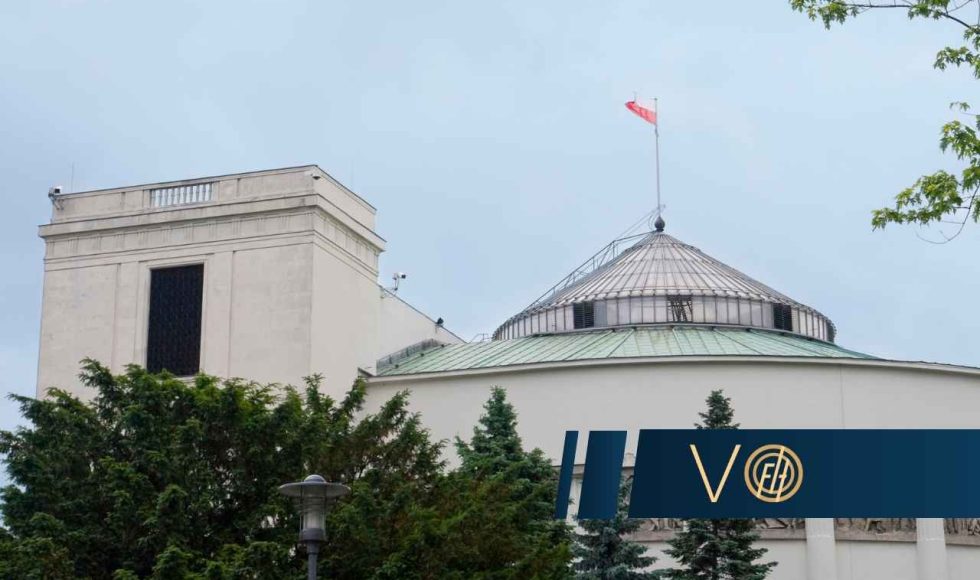 Budynek polskiego Sejmu z charakterystyczną kopułą i polską flagą na szczycie jest częściowo ukryty za drzewami i krzewami