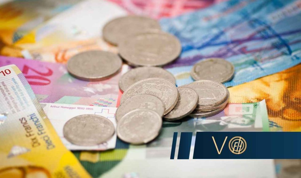 Na tle kolorowych banknotów franków szwajcarskich leży kilka srebrnych monet
