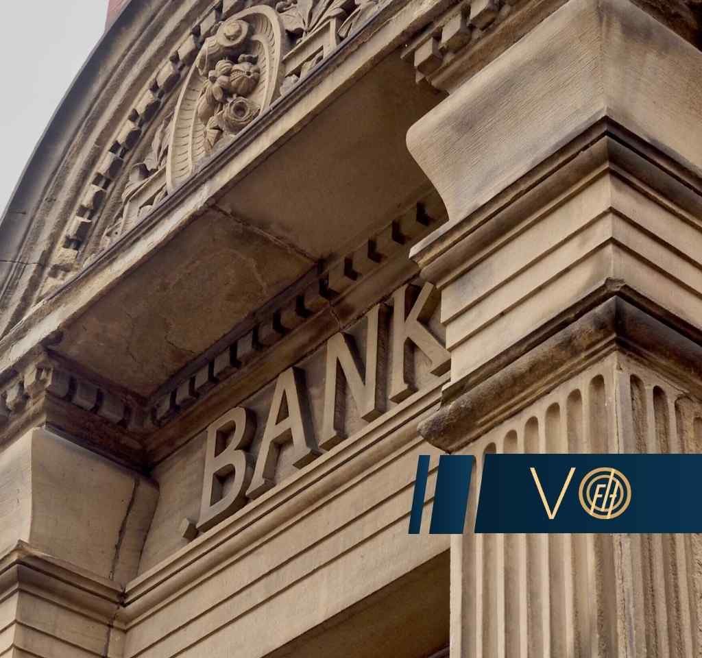 Zbliżenie na kamienną, klasyczną fasadę budynku z rzeźbionym detalem i widocznym napisem BANK