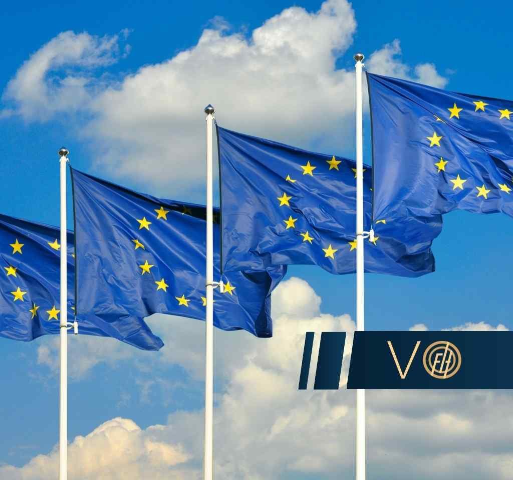 Cztery flagi Unii Europejskiej powiewają na masztach na tle błękitnego nieba z białymi chmurami.