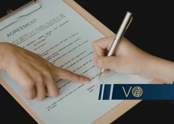 Osoba podpisuje eleganckim piórem dokument opatrzony nagłówkiem „Agreement” umieszczony w podkładce.