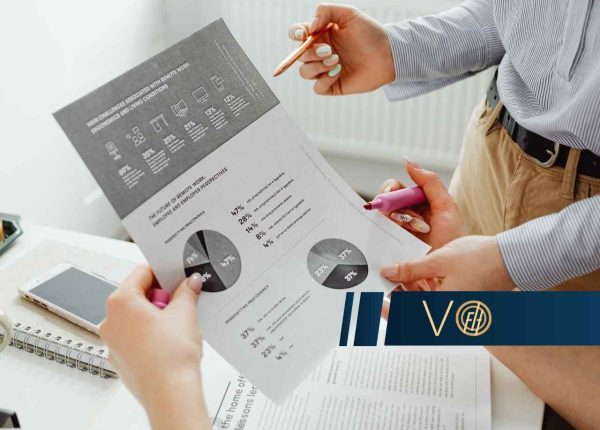 Dwie osoby analizują dokumenty z wykresami kołowymi i danymi statystycznymi, trzymając w dłoniach długopis i różowy zakreślacz.