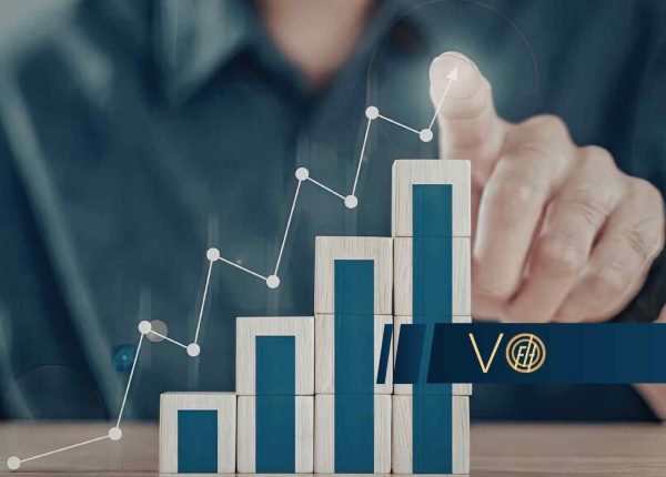 Dłoń wskazuje na rosnący wykres liniowy i słupkowy ułożony z drewnianych klocków, symbolizujący dynamiczny wzrost statystyk.