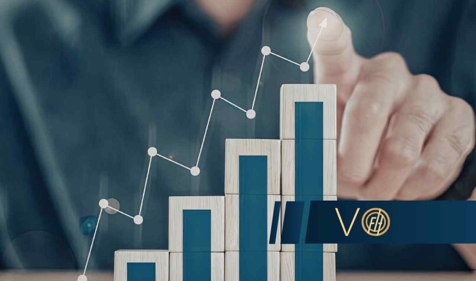 Dłoń wskazuje na rosnący wykres liniowy i słupkowy ułożony z drewnianych klocków, symbolizujący dynamiczny wzrost statystyk.