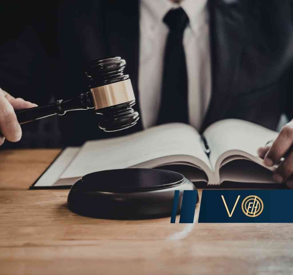 Prawnik w czarnym garniturze i krawacie trzymający młotek sędziowski nad otwartym kodeksem