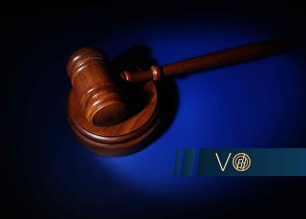 Drewniany młotek sędziowski spoczywający na podstawce, skąpany w punktowym świetle na głębokim, niebieskim tle.