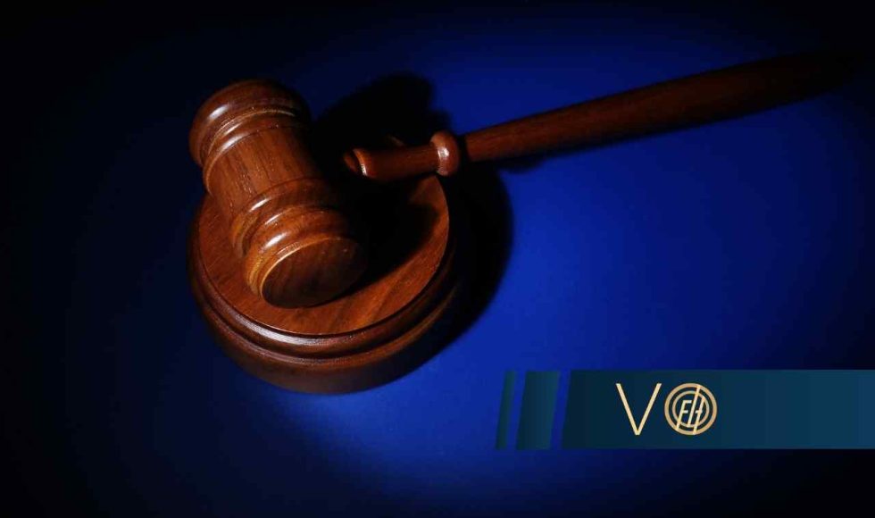 Drewniany młotek sędziowski spoczywający na podstawce, skąpany w punktowym świetle na głębokim, niebieskim tle.