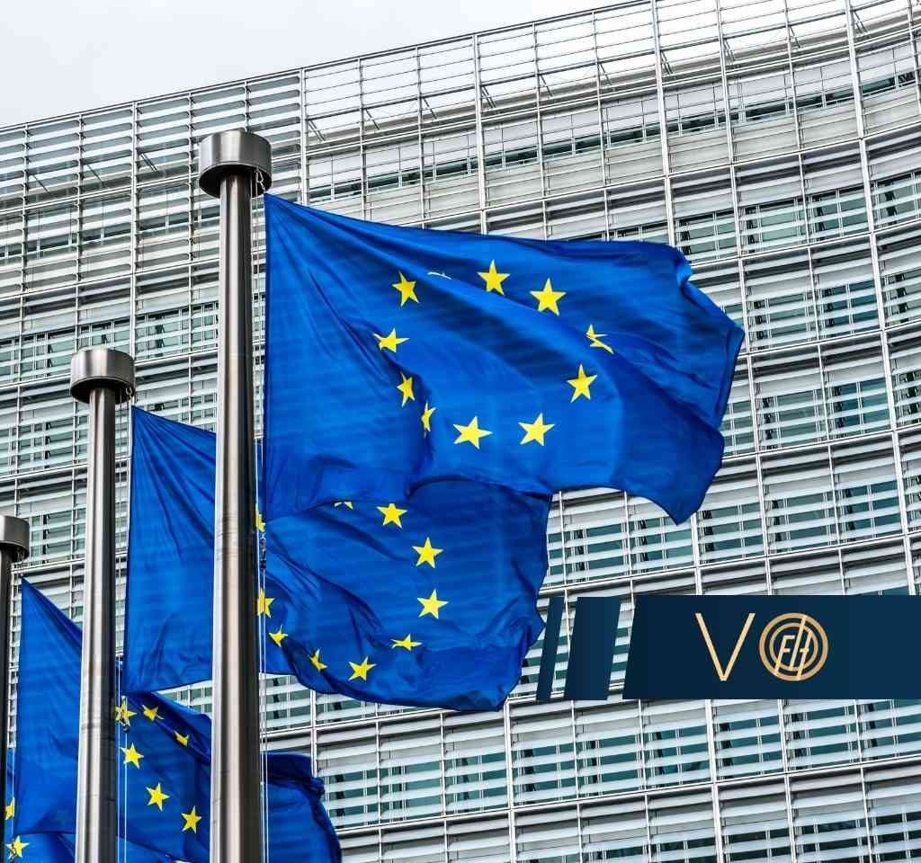 European Union flags waving outside a modern glass office building.