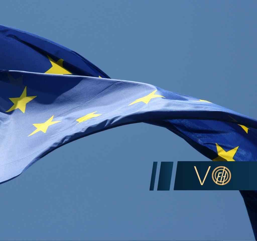 European Union flag waving in the wind with a dark blue banner displaying the letters VO.