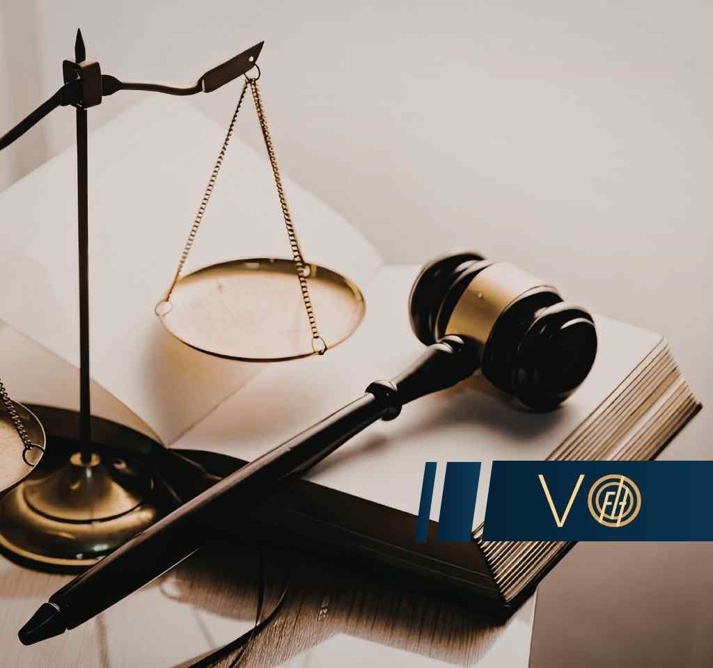 Scales of justice and a wooden gavel resting on an open book, with a blue logo bar across the lower right corner.