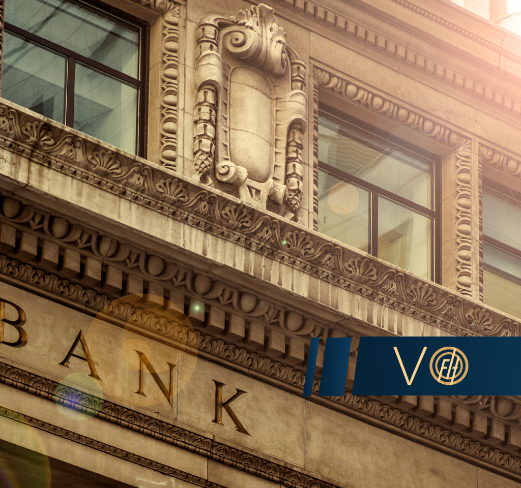 Ornate stone bank facade with decorative carvings and large windows; a blue banner with gold logo crosses the lower right.