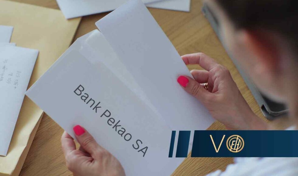 Person holds a white envelope labeled 'Bank Pekao SA' on a wooden desk, with a blue logo bar visible at the bottom right.