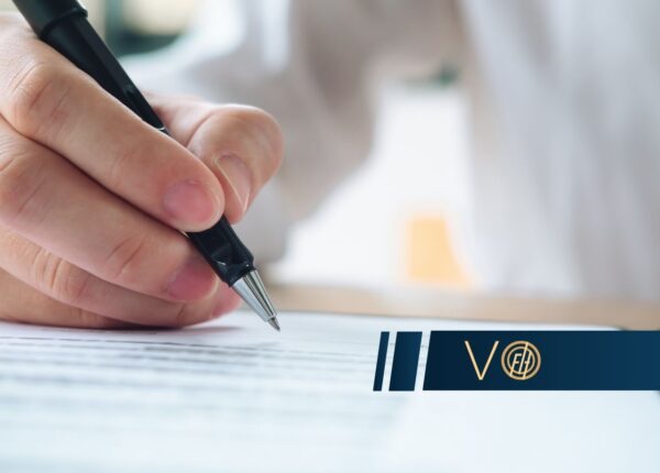 Close-up of a hand signing a document with a pen, a blue logo banner across the bottom.